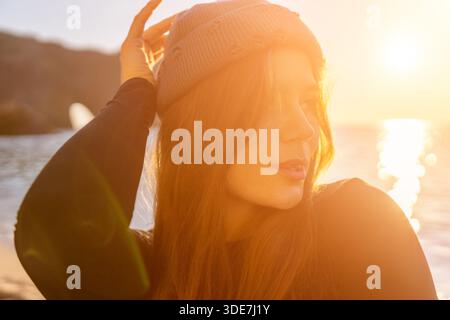 Surfer, Frau, Sonnenuntergang Porträt einer jungen Frau, die eine Beanie trägt und das schöne goldene Stundenlicht am Meer genießt. Stockfoto