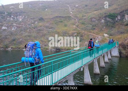 WUHAN, PROVINZ HUBEI, CHINA - 31. OKTOBER 2014: Gruppe von Outdoor-Enthusiasten mit schweren Rucksäcken, die über eine Betonbrücke mit grünem Metall laufen Stockfoto