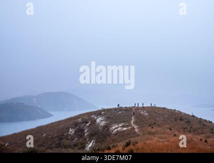 WUHAN, CHINA - 31. OKTOBER 2014: Panoramablick auf den Longwangjian Bergkamm, bedeckt mit trockenem Herbstgras. Winzige Figuren von Wanderern sind zu sehen Stockfoto