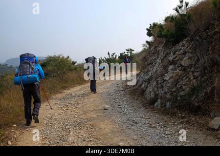 WUHAN, CHINA - 31. OKTOBER 2014: Rückansicht von Wanderern mit großen Rucksäcken auf unterschiedlichem Gelände. Die Bilder zeigen Trekking auf felsigen Schotterwegen, Stockfoto