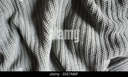 Nahaufnahme einer Strickdecke oder eines Pullovers in einer hellgrauen, salbeigen Farbe. Gemütlicher, warmer Hintergrund für Herbst-, Winter- oder Urlaubskonzepte. Handgestrickter, vertikaler Rippnaht. Warmes Tuch. Stockfoto