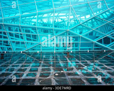 Abstrakte Ansicht einer modernen Glasarchitektur, die sich im Wasser spiegelt und ein blaues geometrisches Gittermuster erzeugt. Das Bild vermittelt Technologie, inno Stockfoto