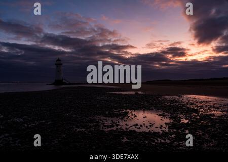 Point of Ayr Lighthouse (Talacre Lighthouse) bei Sonnenaufgang, mit warmem Licht, das über Gezeitenbecken und die Kieselküste unter dramatischer Wolke reflektiert Stockfoto