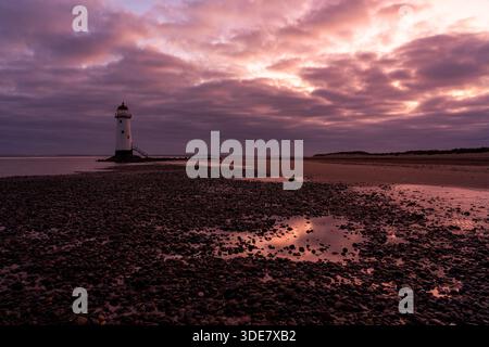 Point of Ayr Lighthouse (Talacre Lighthouse) bei Sonnenaufgang, mit warmem Licht, das über Gezeitenbecken und die Kieselküste unter dramatischer Wolke reflektiert Stockfoto