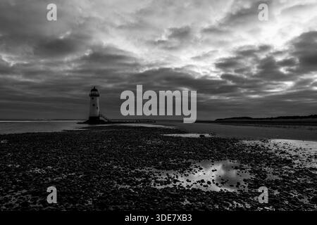 Schwarz-weiß-Blick auf den Point of Ayr Lighthouse (Talacre Lighthouse), der vor der Küste zwischen Kieselsand und Gezeitenbecken unter dramatisch bewölkten Gewässern steht Stockfoto
