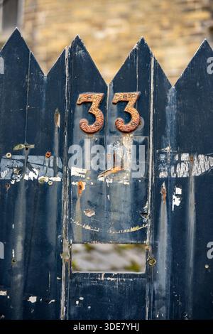Die Nummer 33 dreiunddreißig auf einem alten hölzernen Tor mit gewölbter Spitze, Nahaufnahme eines alten hölzernen Tors mit der Nummer 33 und offenem Briefkasten. Stockfoto