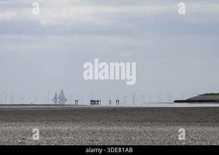 Menschen und Segelschiffe im Wattenmeer bei Ebbe mit Windturbinen am Horizont, Menschen am Strand mit Booten und Windturbinen im dist Stockfoto