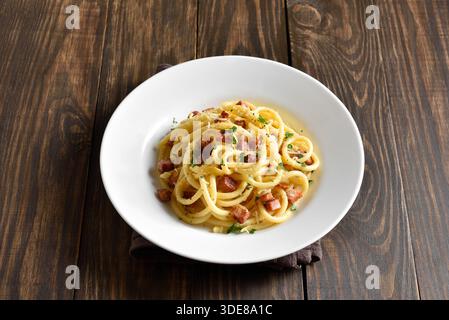 Carbonara-Pasta, Spaghetti mit knuspriger Pancetta und schwarzem Pfeffer auf weißer Platte auf rustikalem Holzhintergrund. Traditionelle italienische Küche. Nahansicht Stockfoto