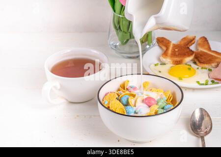 Osterfrühstück Müsli, Cornflakes mit Osterschokoladeneiern und Zuckerstreuseln, Milch oder Joghurt in Cornflakes Golden Breakfast Müsli Portion Stockfoto