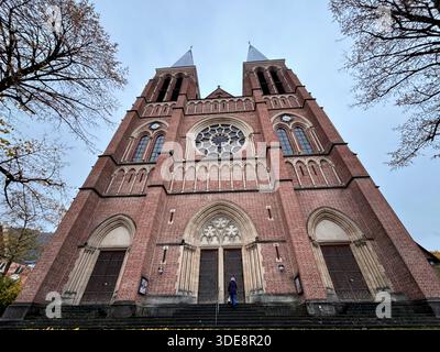 Flacher Blick auf eine Ziegelfassade mit zwei Türmen und kreisförmigen Buntglasfenstern, architektonischen Details und Symmetrie. Stockfoto