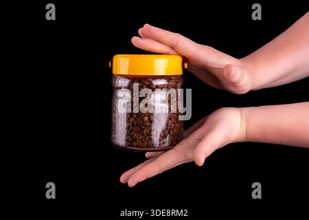 Kaffeebohnen in der Glasdose, die männliche Hände halten. Isoliert auf schwarzem Hintergrund. Stockfoto