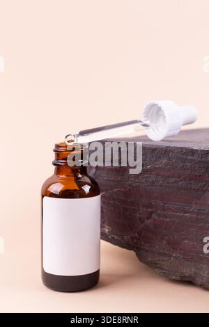 Unmarkierte braune Glasflasche mit Tropfdeckel auf beigefarbenem Hintergrund auf dem Stein. Mock-up von Gesichtsserum bei Sonnenstrahlen. Nahaufnahme, Kopierbereich Stockfoto