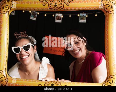Zwei Frauen posieren für ein Bild vor einem gelben Rahmen. Eine der Frauen trägt eine Sonnenbrille Stockfoto
