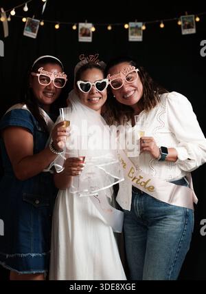 Drei Frauen posieren für ein Foto. Einer trägt ein weißes Kleid und einen weißen Schleier. Die anderen beiden Frauen tragen eine Sonnenbrille Stockfoto