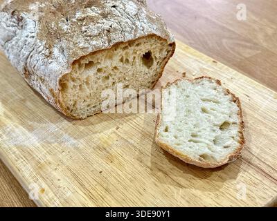 Ein Stück frisches, hausgemachtes, knuspriges Sauerteigbrot mit einer Scheibe, nachdem es auf einem Brett geschnitten wurde Stockfoto