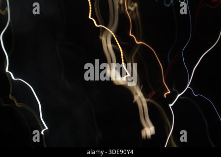 Ein abstraktes Langzeitfoto mit minimalistischen weißen und goldenen Lichtspuren, die vertikal vor einem massiven schwarzen Hintergrund fließen. Stockfoto