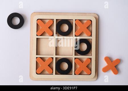 Blick von oben auf ein hölzernes Noughts and Croses Spiel mit orangefarbenen X- und schwarzen O-Stücken auf einer weißen Oberfläche. Strategie- und Spielkonzept. Stockfoto