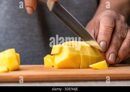 Nahaufnahme der Hände, die eine rohe Kartoffel mit einem Gemüseschäler über einem Schneidebrett schälen. Küchenchef schneidet von Hand frische Kartoffeln zum Kochen auf einem Tisch. Schneiden Stockfoto