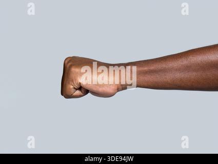 Hand eines afroamerikanischen Mannes mit geballter Faust. Afrikanische Fausthand. Die Fausthand gibt einen Schlag, die Faust über grauem Hintergrund. Die erhobene Faust eines afrikanischen Mannes Stockfoto