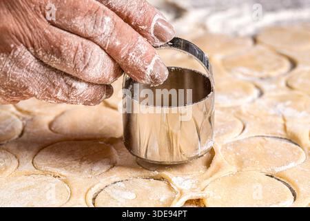 Zubereitung des Teigs zum Backen, ein großes Stück des Teigs liegt auf dem Tisch und der Koch schneidet kleine Kreise mit eiserner Form aus Stockfoto