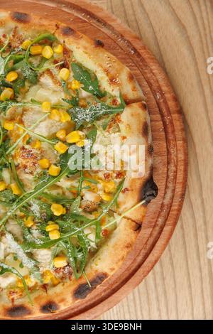 Die Leute versammeln sich um einen Tisch, um sich eine frisch gebackene Pizza zu teilen. Die Pizza bietet einen Topping aus süßem Mais und frischem Rucola. Die warme, einladende Atmosphäre Stockfoto