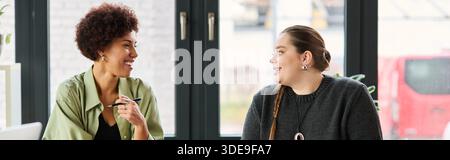 Zwei weibliche Führungskräfte führen in einer lebhaften Diskussion in einer hellen Büroatmosphäre, Banner Stockfoto