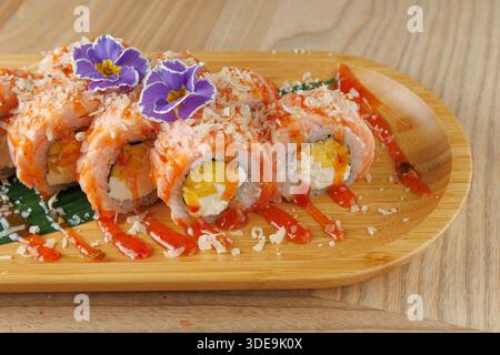Sushi-Brötchen sind ordentlich auf einem Holzteller angeordnet. Die Brötchen sind mit Lachs, Eiern gefüllt, mit Soße belegt und mit essbaren Blüten garniert. Pl Stockfoto