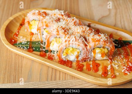 Sushi-Brötchen werden auf eine Holzplatte gelegt. Die Brötchen werden mit bunten Saucen und Garnituren belegt. Der Hintergrund deutet auf eine warme Atmosphäre hin Stockfoto