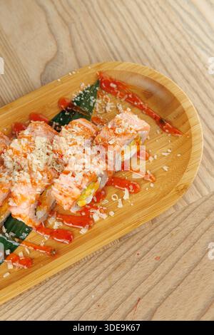 Sushi-Brötchen werden mit frischen Zutaten kombiniert und mit würziger Soße auf einem Holzteller getränkt. Die Umgebung ist zwanglos, perfekt zum Genießen einer Mahlzeit. Stockfoto