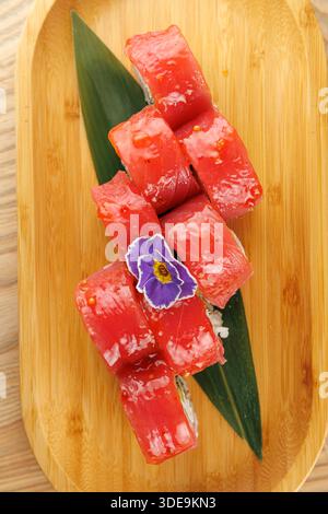 Frische Thunfisch-Sushi-Brötchen sind ordentlich auf einem Holzteller angeordnet. Ein grünes Blatt und eine kleine dekorative Blume ergänzen die Präsentation. Perfekt zum Genießen Stockfoto