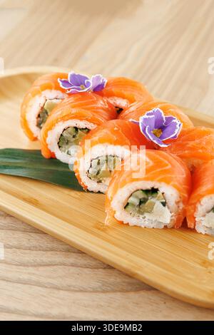 Bunte Sushi-Brötchen sind ordentlich auf einem Holzteller angeordnet. Die Brötchen enthalten Fisch und Gemüse und sind zur Dekoration mit essbaren Blüten garniert Stockfoto