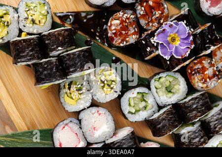 Sushi-Brötchen sind kunstvoll auf einem Holzbrett angeordnet. Texturen und Farben verschiedener Typen werden hervorgehoben und zeigen die kulinarische Handwerkskunst. Stockfoto