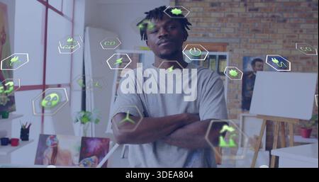 Stehender Mann mit grauem T-Shirt, Blick auf Kamera im Kunststudio, Staffeleien und grüne Energie-Ikonen Stockfoto