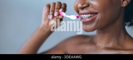 Frau putzt während der morgendlichen Routine Zähne, während sie im Badezimmer eine Zahnspange trägt Stockfoto