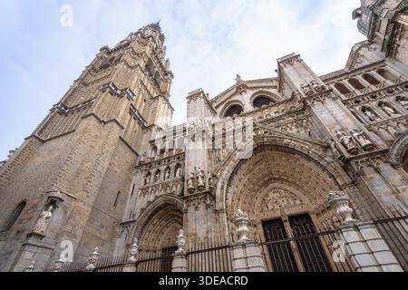 Gotische Fassade der Primatial Kathedrale der Heiligen Maria von Toledo mit komplizierten Steinschnitzereien und einem hohen Glockenturm unter hellem Himmel. Stockfoto