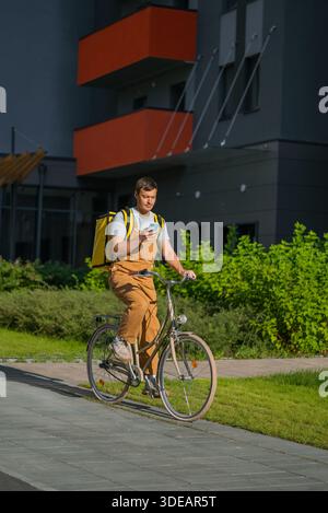 Fahrradkurier, der Lebensmittel auf einem Fahrrad in einer urbanen Umgebung liefert, auf einem Mobiltelefon nach Wegbeschreibungen sucht, repräsentiert die Gig Economy und den modernen Lieferservice Stockfoto