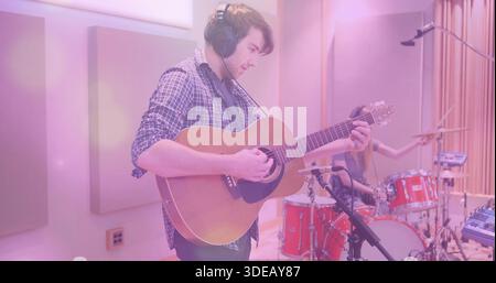 Gitarrist in kariertem Hemd, Kopfhörer, Akustikgitarre im Studio, rotes Schlagzeug Stockfoto