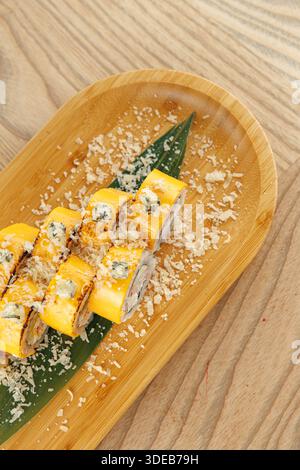 Sushi-Brötchen sitzen auf einem Bambusteller, der mit geriebener Kokosnuss belegt und auf einem grünen Blatt platziert wird. Die Einstellung zeigt einen einfachen Holztisch, der in Japan üblich ist Stockfoto