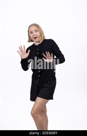 Verängstigte oder überraschte Frau, die in einem schwarzen Kleid zurückschreckt. Stockfoto