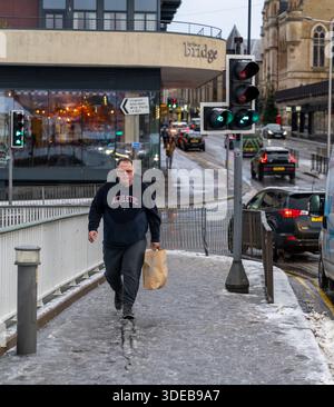 Ein Mann läuft zügig auf einem schlammigen, mit Schnee bedeckten Pflaster, während er eine Tasche trägt. Diese Szene findet in der Nähe der Ness Bridge statt. Es ist Winter in Inverness. Stockfoto
