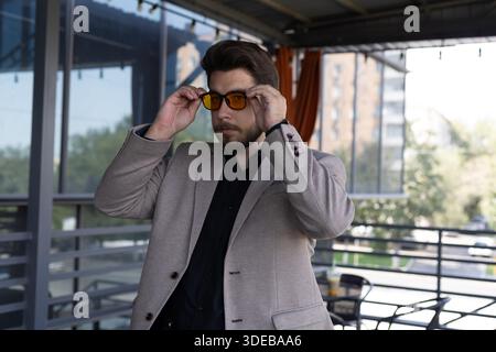 Ein Mann in einer Jacke, der seine Sonnenbrille draußen anpasst. Stockfoto