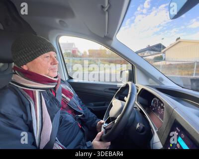 Aktives Altern als älterer Lebensstil eines älteren Mannes, der bei Tageslicht ein modernes Auto fährt, Winterkleidung trägt, ruhiger fokussierter Ausdruck im Auto, alltäglicher M Stockfoto