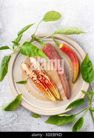 Lange rote Elefanten-Pfeffer-Chilis mit strukturierter Haut und grünen Stielen auf einer Keramikschale. (Capsicum annuum) Paprika, eine aufgeschnitten, die Wärme darstellt Stockfoto
