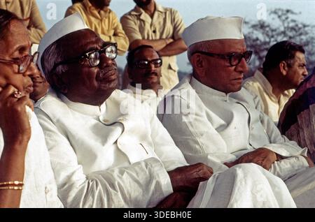 Jagjivan RAM und Morarji Desai sitzend in einer Reihe bei einer öffentlichen Veranstaltung, umgeben von weiteren Personen. Beide tragen traditionelle weiße Kleidung und Kopfbedeckungen. Indien, 1970er. Stockfoto