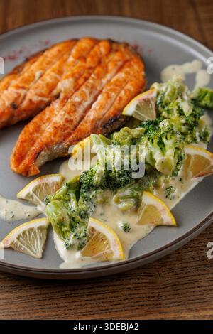 Auf dem Gericht werden gegrillte Lachsfilets mit Brokkoli in einer cremigen Sauce und mit Zitronenscheiben garniert. Das Essen wird auf einem Teller und serviert Stockfoto