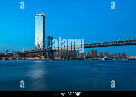 Die berühmte Manhattan Bridge überspannt den East River während der ruhigen blauen Stunde und verbindet Brooklyn mit Lower Manhattan. Stockfoto
