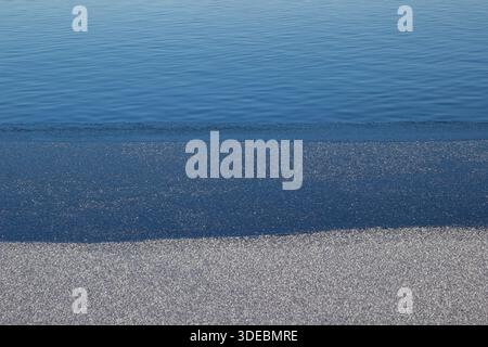 Drei Streifen eines eiskalten Flusses: Blaues Wasser, ein Rand aus blauem Eis, weißer Schnee auf der Oberfläche des Eises Stockfoto