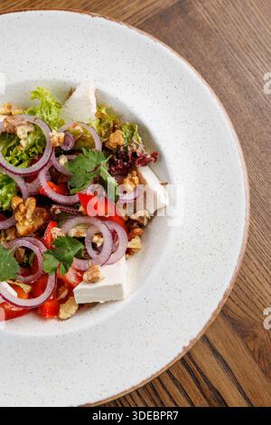 Ein farbenfroher Salat umfasst Hühnerwürfel, Salat, Tomaten, Zwiebeln und Walnüsse. Er wird mit Koriander garniert und in einer runden Schale auf einem Holz präsentiert Stockfoto