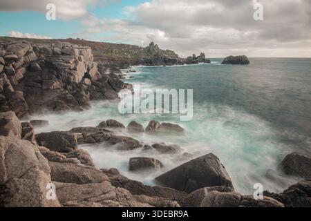 Eine lange Exposition von Wellen, die bei Sonnenuntergang gegen ein felsiges Ufer brechen, Penninis, St Mary's, Isles of Scilly, Oktober 2015 Stockfoto