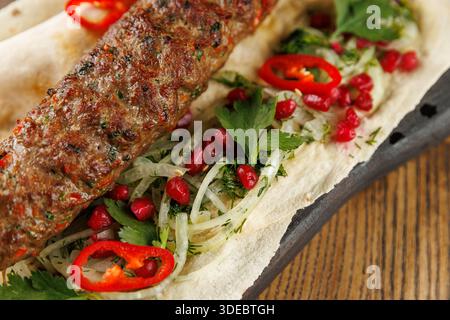 Eine Mahlzeit besteht aus gegrillten Kebabs auf Fladenbrot mit frischen Kräutern, geschnittenen Zwiebeln, Granatapfelkernen und roten Chilischoten. Jeder Inhaltsstoff fügt Farbe und hinzu Stockfoto